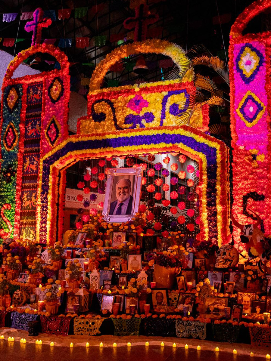 A candlelit Día de los Muertos ofrenda decorated with marigolds, photographs and traditional remembrance items.